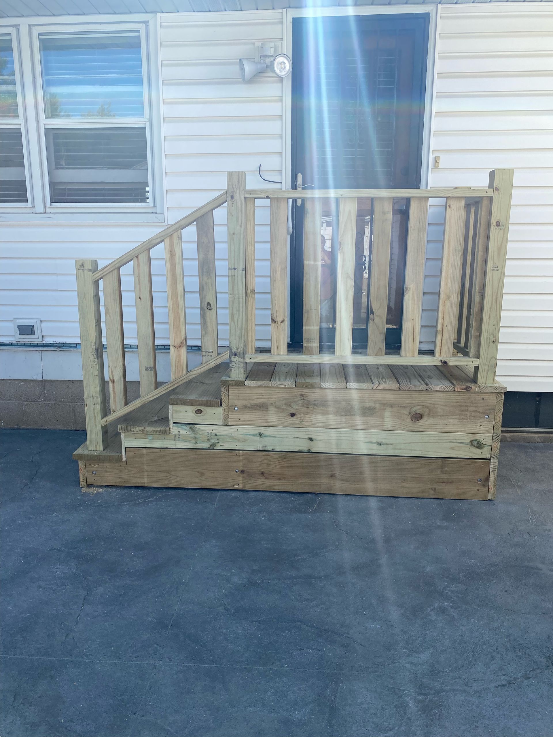 Wooden porch ramp and steps leading to a house entrance beside a white exterior wall