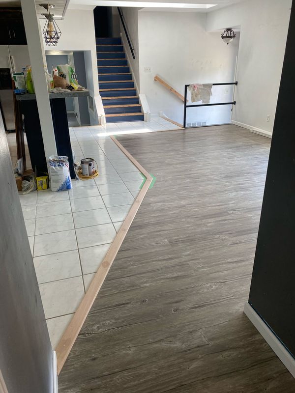 Indoor hallway with tiled and carpeted floors leading to a staircase and railing.