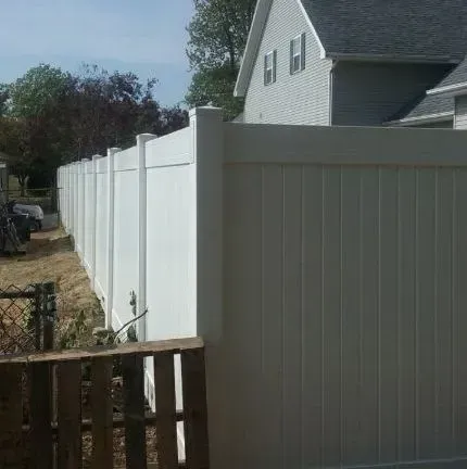 A white vinyl fence is surrounding a house with a wooden gate.