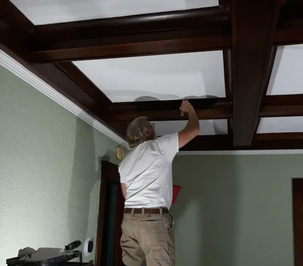 A man in a white shirt is working on a wooden ceiling