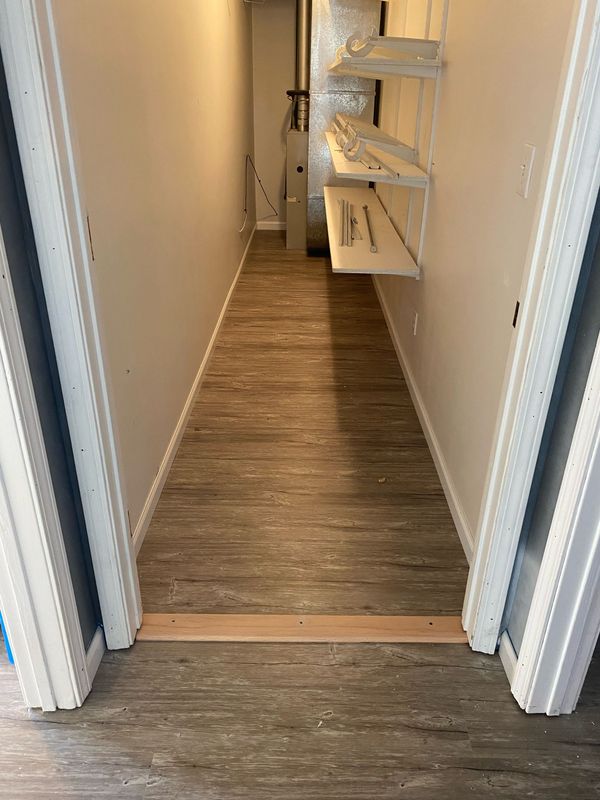 Narrow hallway with wood-look flooring and white walls, leading to a small staircase with open shelving on the right