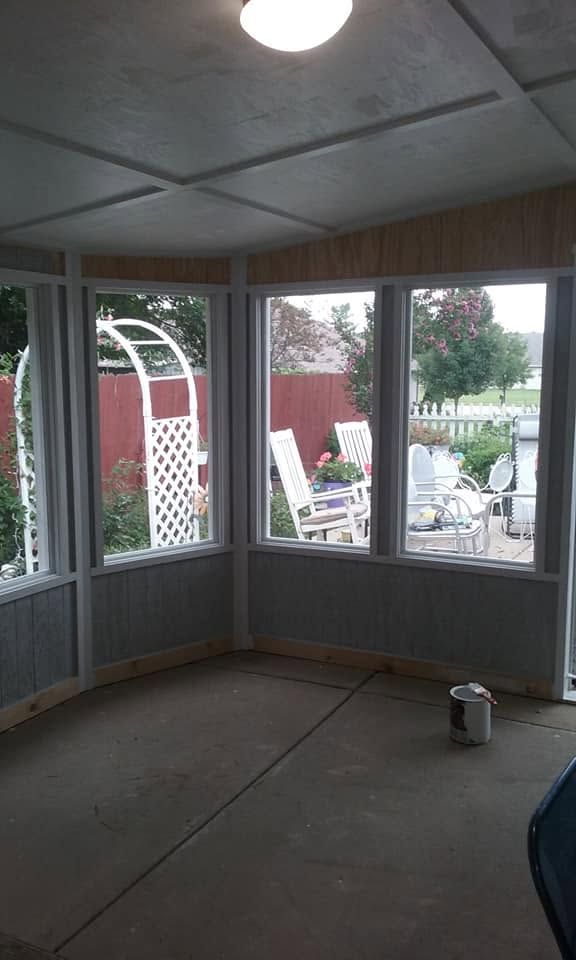 Screened-in porch with white chairs, red fence, and a paint bucket on the floor.