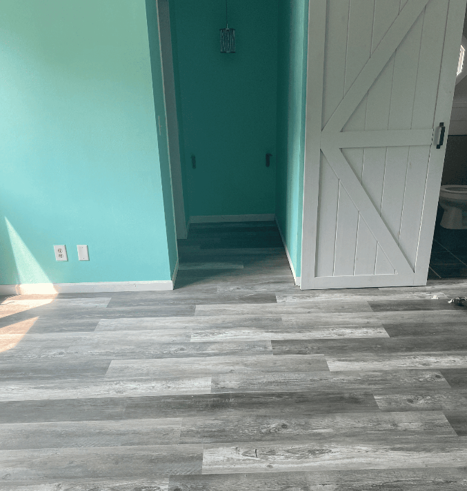 Empty room with teal walls, gray wood flooring, and an open white door leading to a hallway.