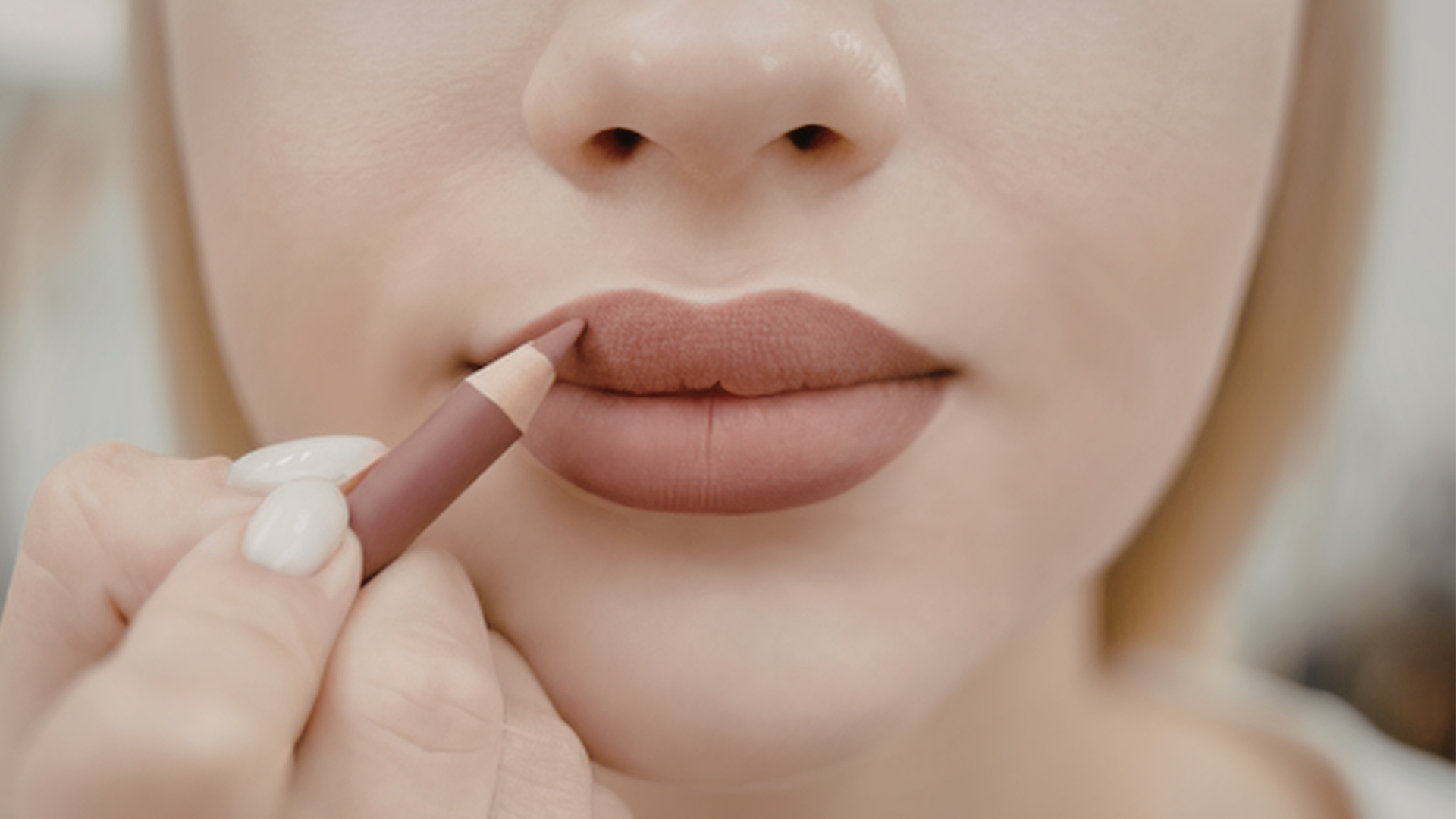 Applying nude lipstick to a person’s lips close-up