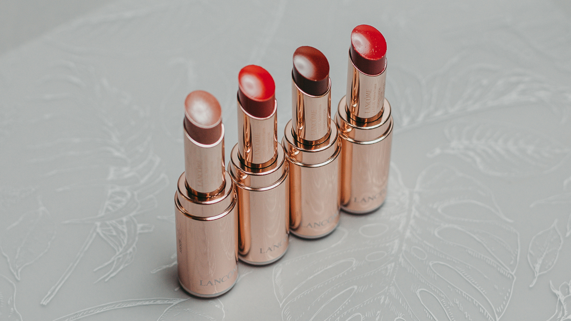 Four lipsticks in rose gold tubes, each with a different red or nude shade.