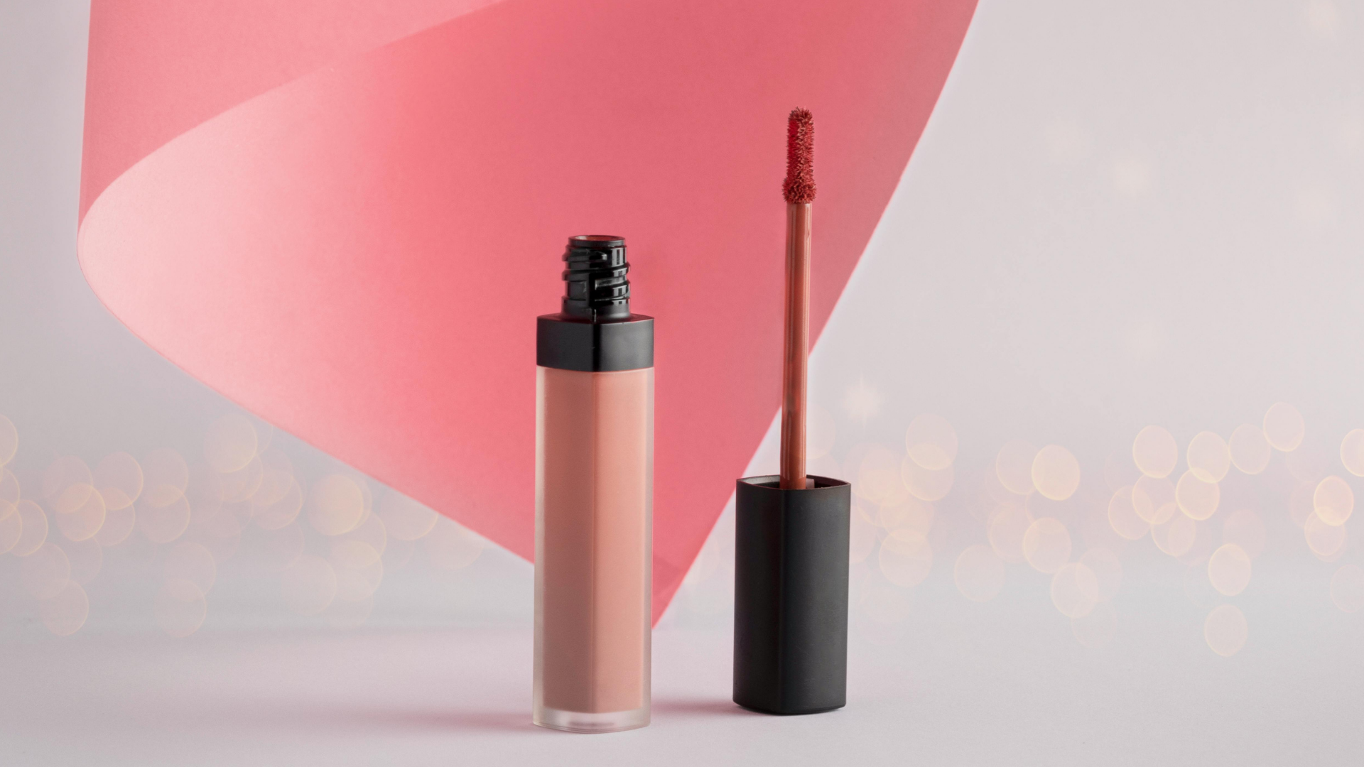 Pink lip gloss tube and applicator on a soft pink background with bokeh lights