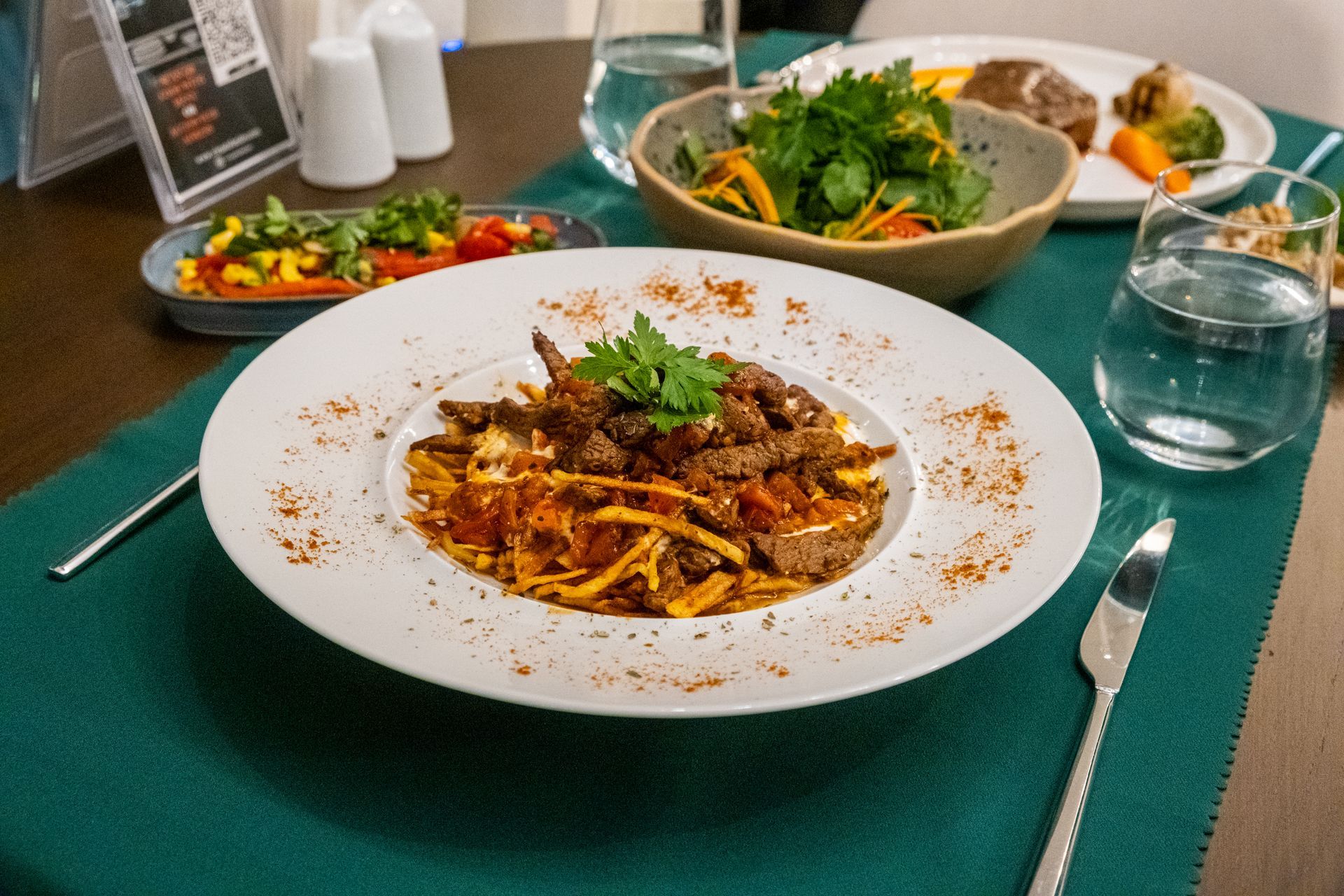 Bir kase salatanın yanındaki masada bir tabak yemek duruyor.