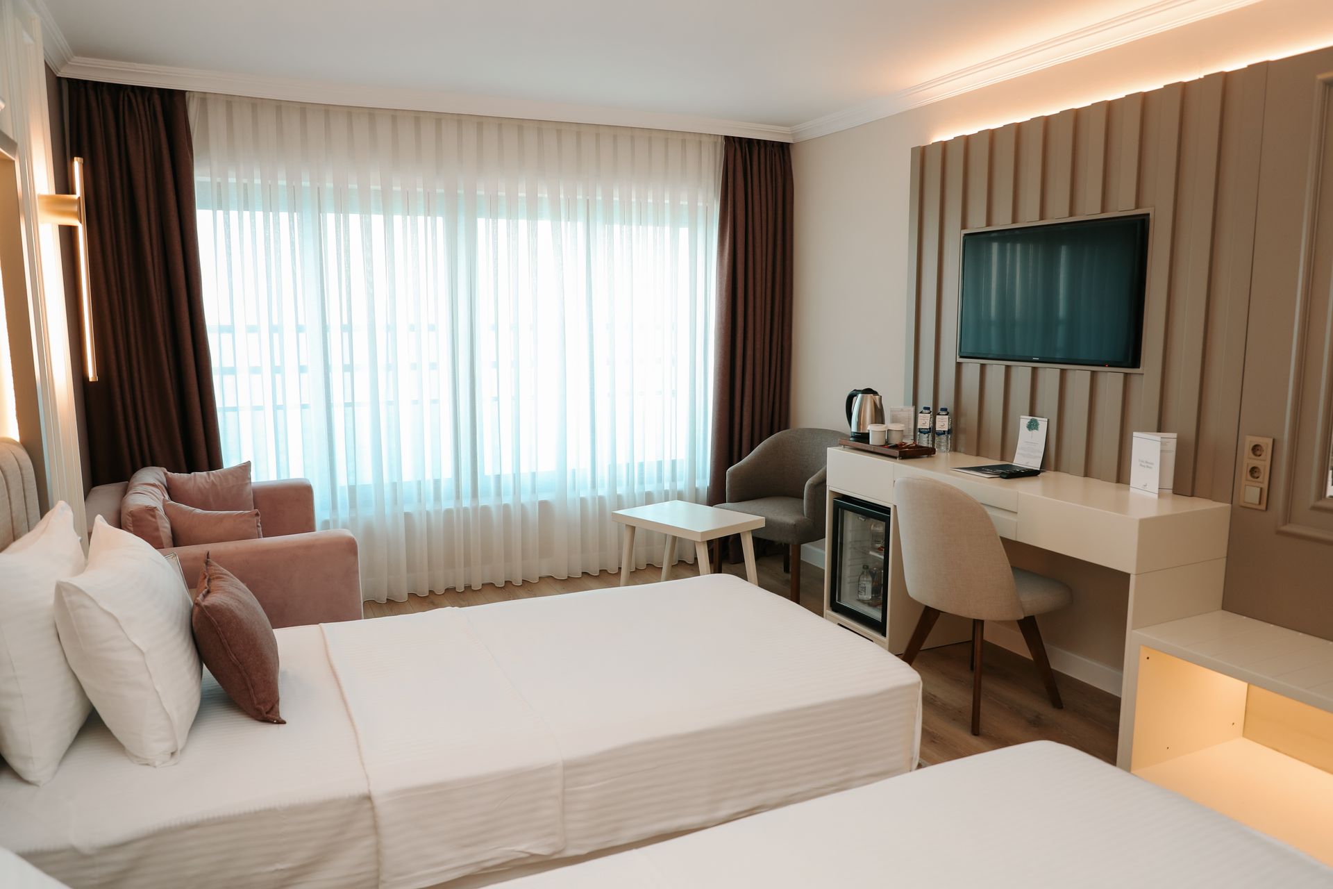 Iki yatak, bir kanepe, bir çalışma masası ve bir televizyonun bulunduğu bir otel odası.