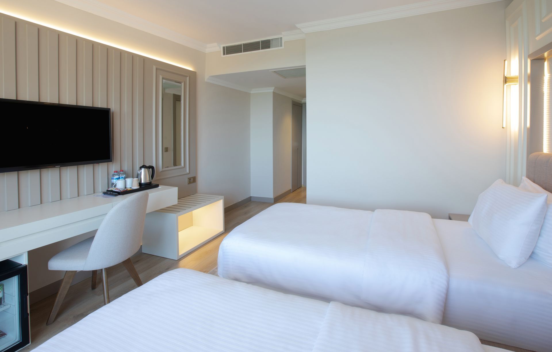 Iki yataklı, çalışma masası ve düz ekran televizyonlu bir otel odası.