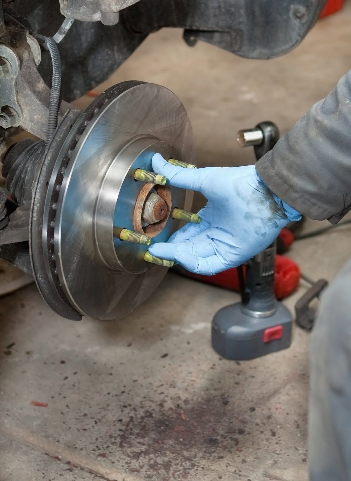 Gloved hands installing a brake rotor on a car wheel hub in a garage | Frontier Auto Center