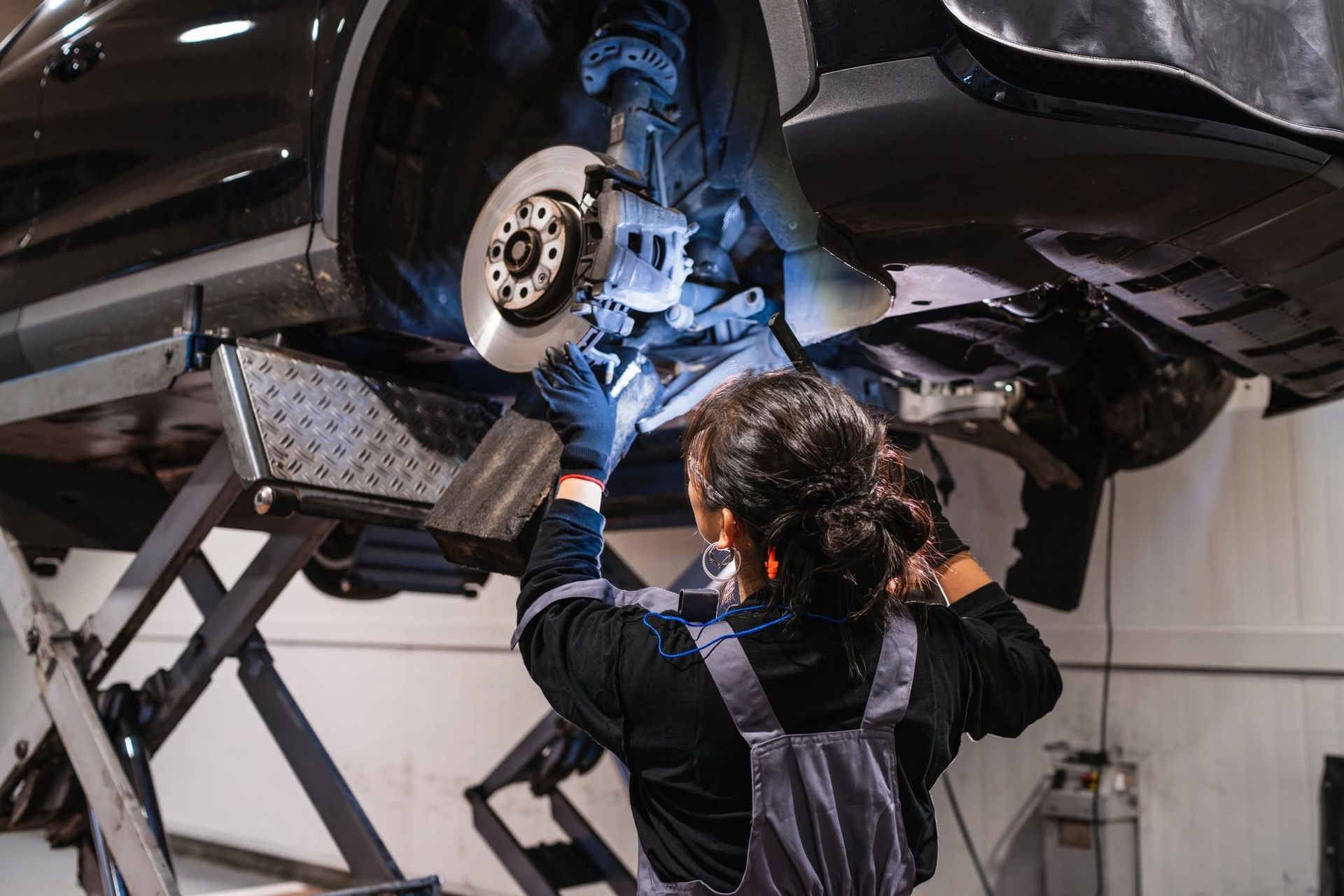 Mechanic inspecting a car’s front wheel and brake assembly on a lift in an auto shop | Frontier Auto Center