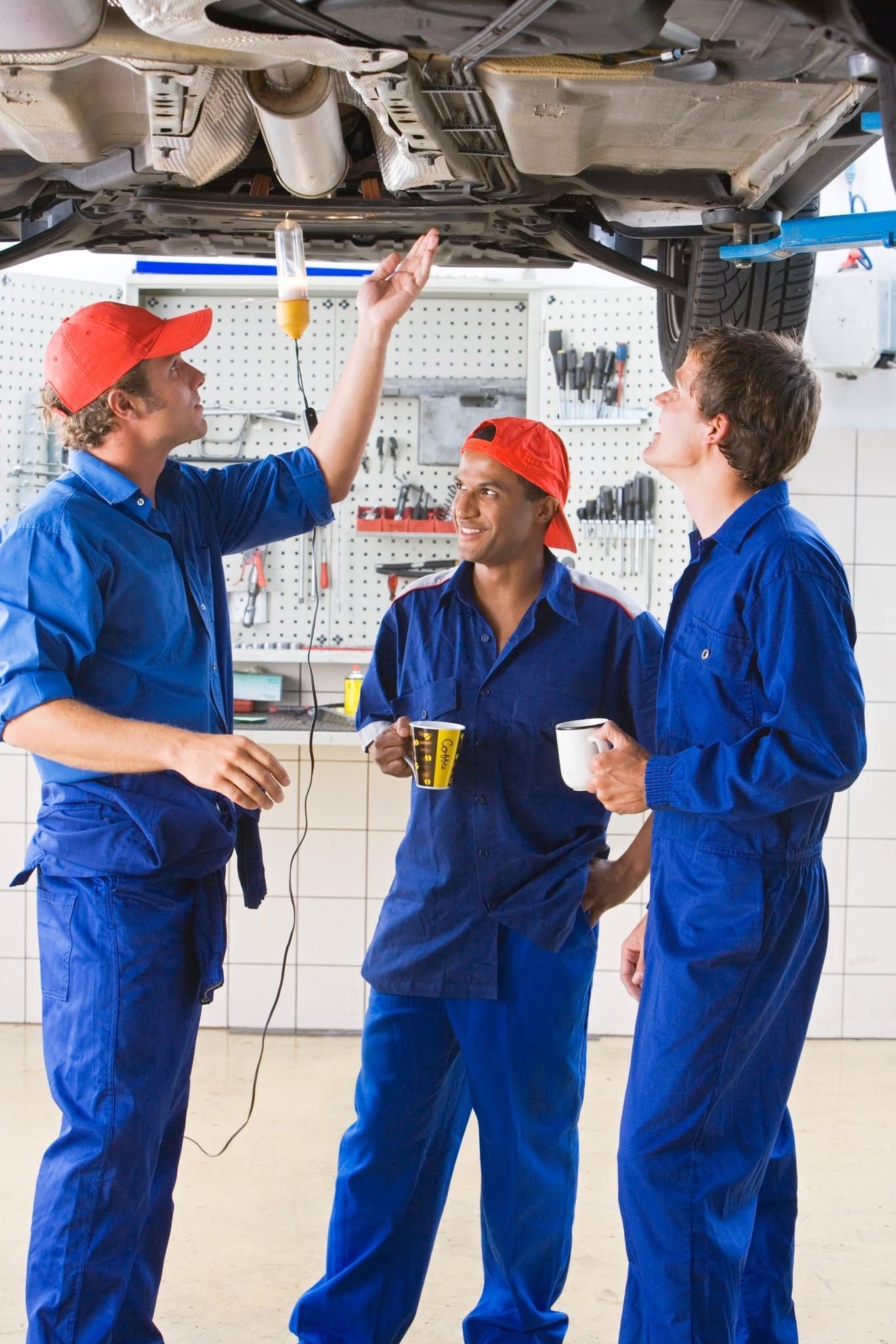 Three mechanics in blue coveralls inspect a car’s underside in a garage | Frontier Auto Center