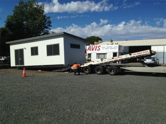 Man Loading a 1-bedroom Portable House Onto the Rear Tail of a Truck — OSM Transportables In Dubbo, NSW