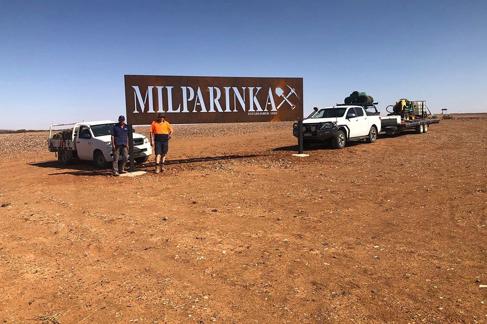 Two Men Standing Beside the Sign 'milparinka' With Two Trucks Parked Nearby — OSM Transportables In Dubbo, NSW