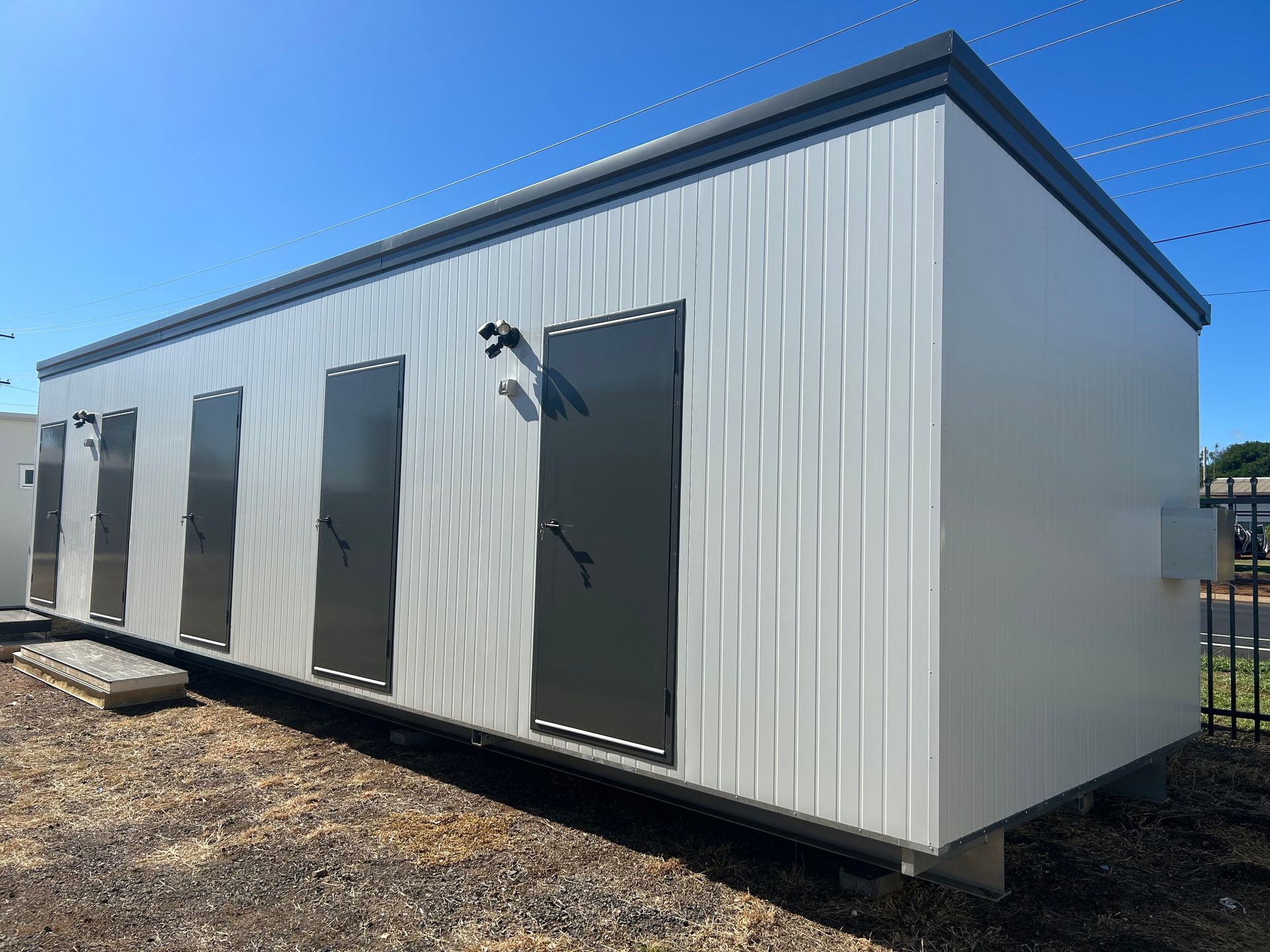 A Light Gray, Rectangular Prefabricated Building With Four Dark Doors — OSM Transportables In Dubbo, NSW