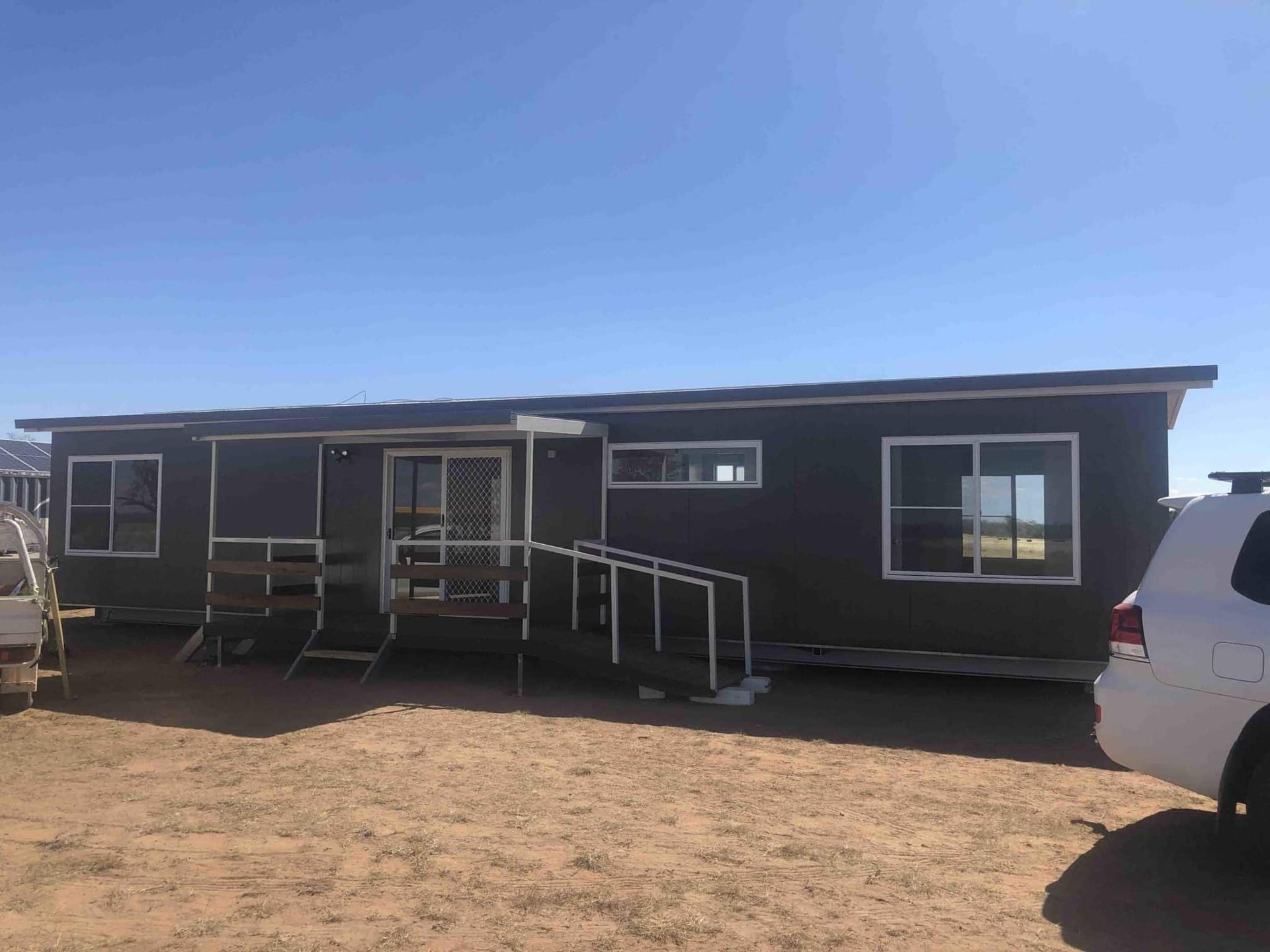 Long Black Portable House With a Small Porch and a Car Parked Nearby — OSM Transportables In Dubbo, NSW