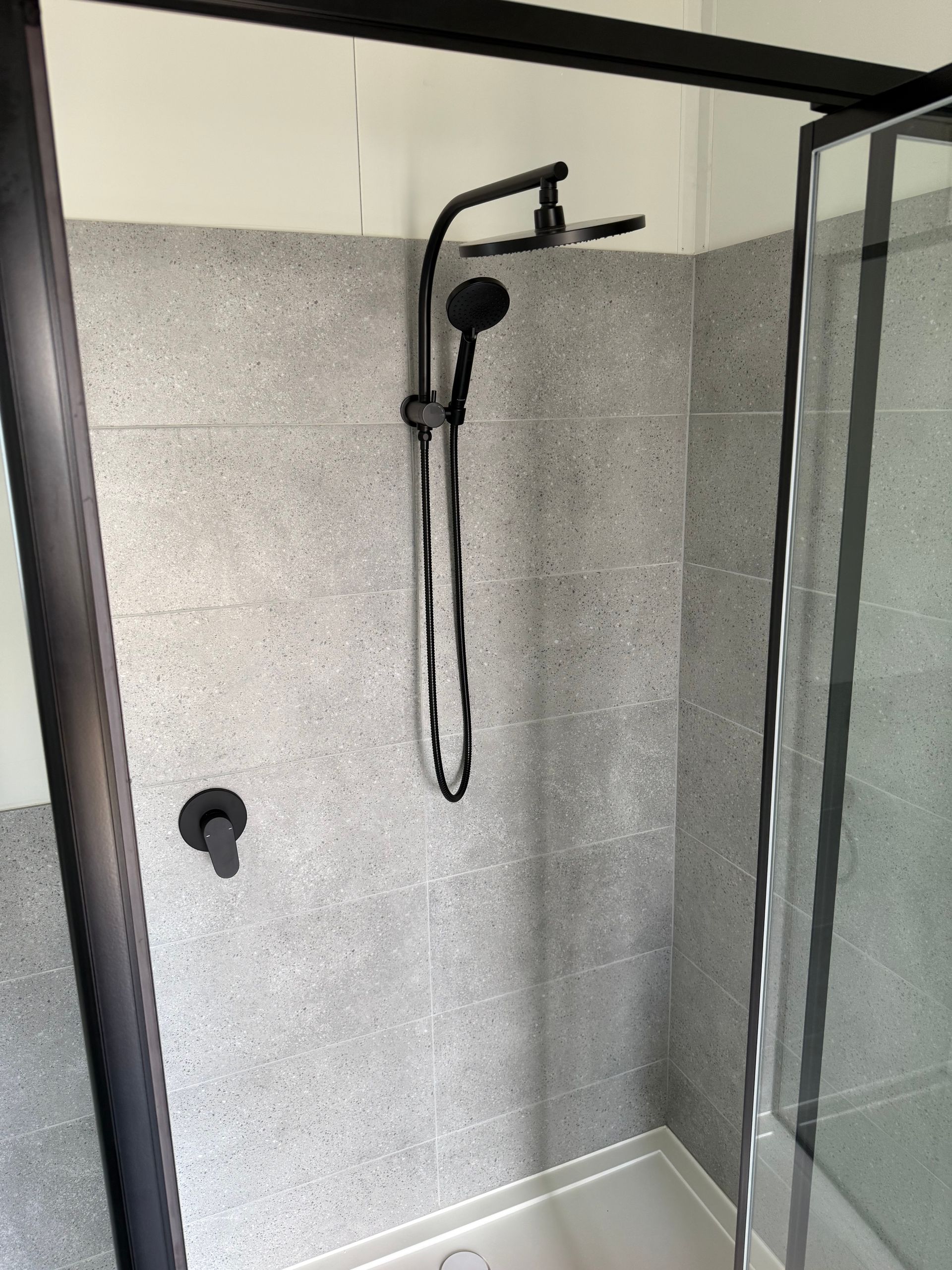 A Shower Stall With Light Gray Tiled Walls, a Black Shower Head — OSM Transportables In Dubbo, NSW