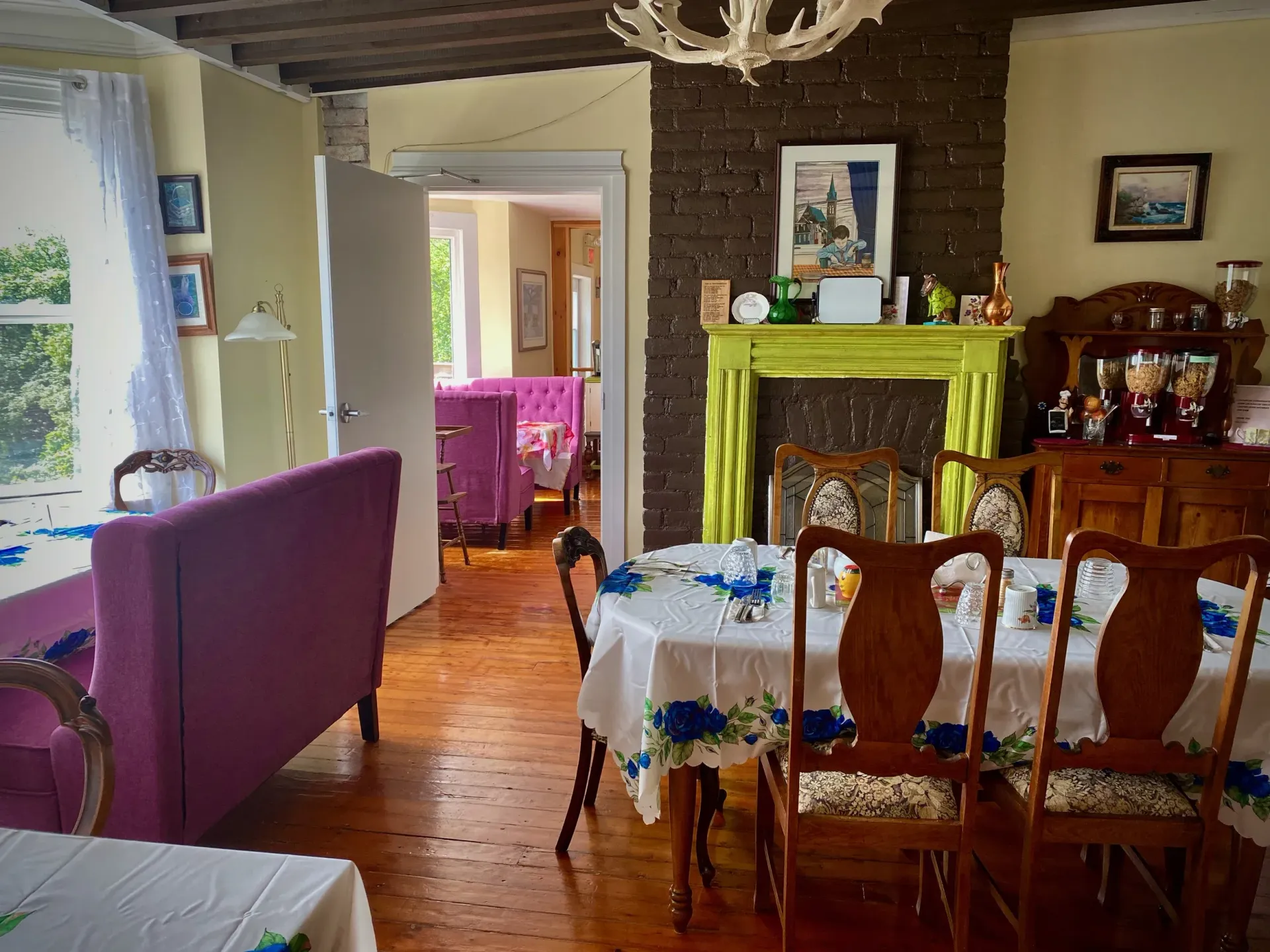 Dining room with purple sofa, table set for dining, green fireplace, and antique furniture.