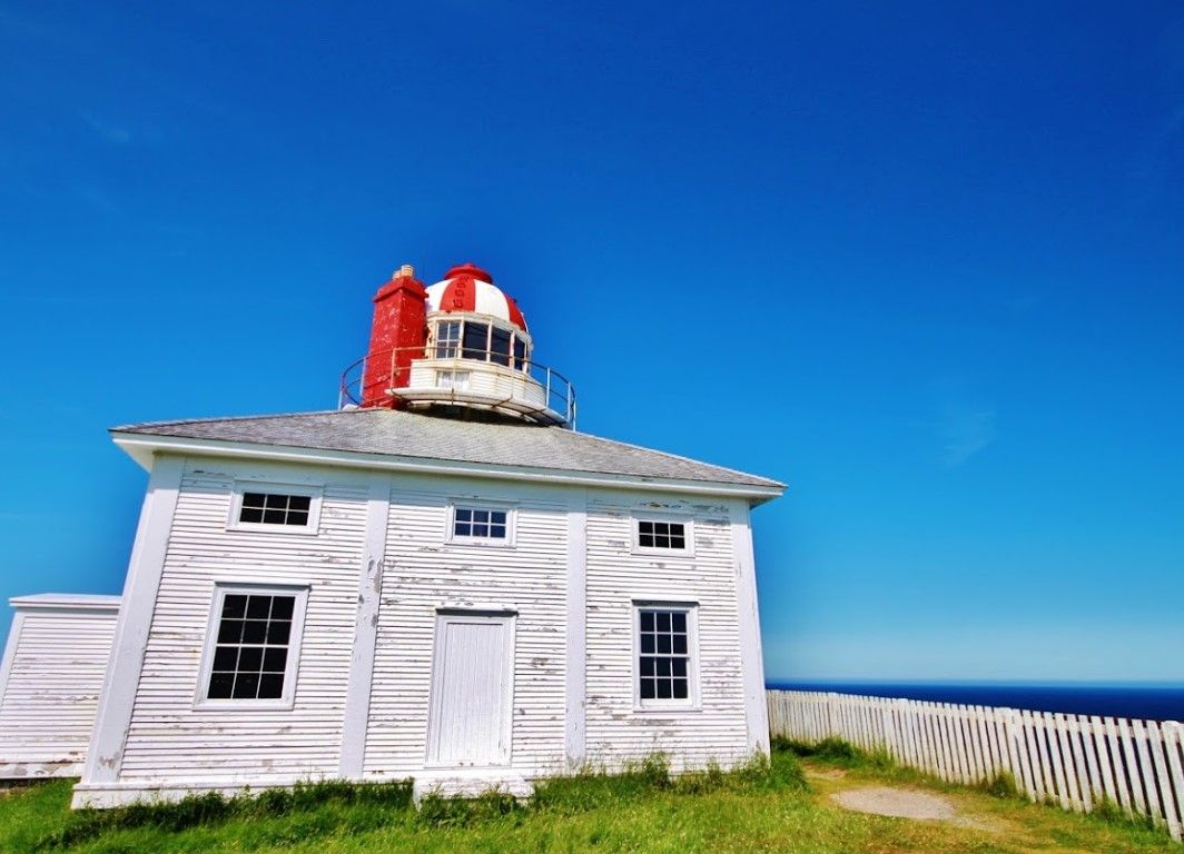 White lighthouse with red top against bright blue sky and ocean.
