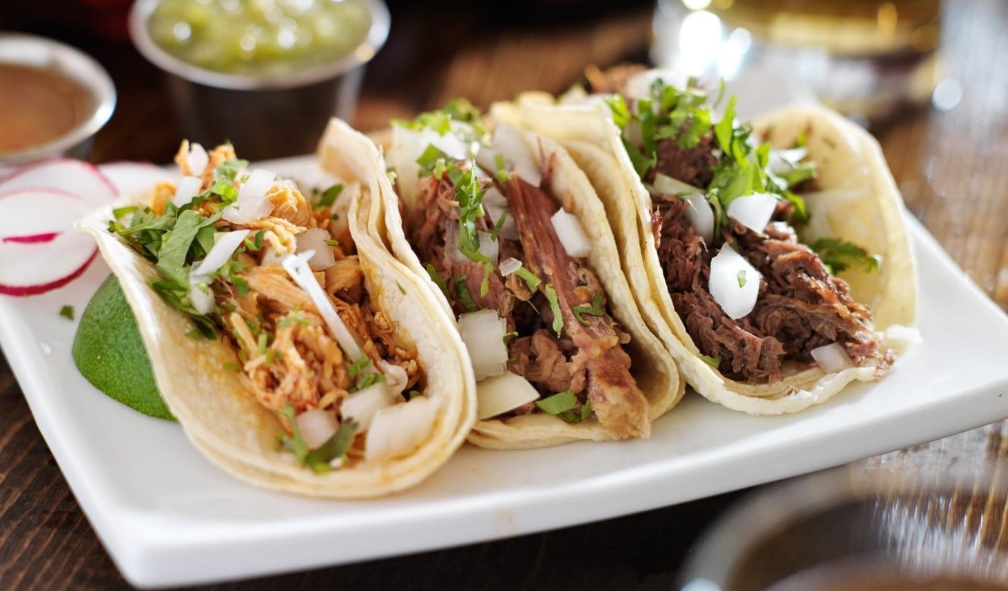 Three tacos on a white plate, filled with meat, cilantro, and onion.