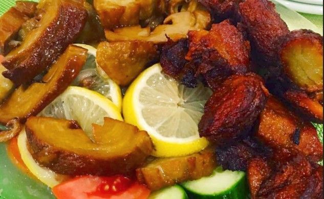 A plate of cooked food including fried root vegetables, mushrooms, lemon slices, and tomatoes.