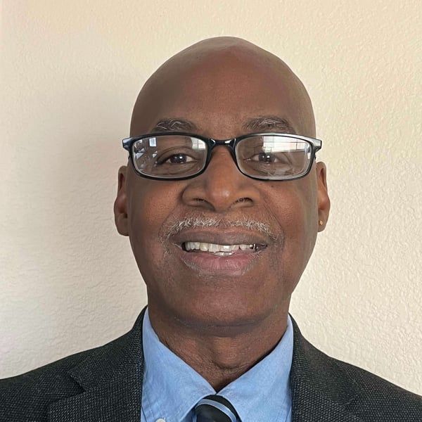 A bald man wearing glasses and a suit and tie is smiling for the camera.