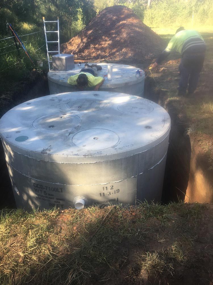 Two Large Gray Water Tanks in a Trench, With Two Workers Nearby — VR Marsden Plumbing in Urunga, NSW