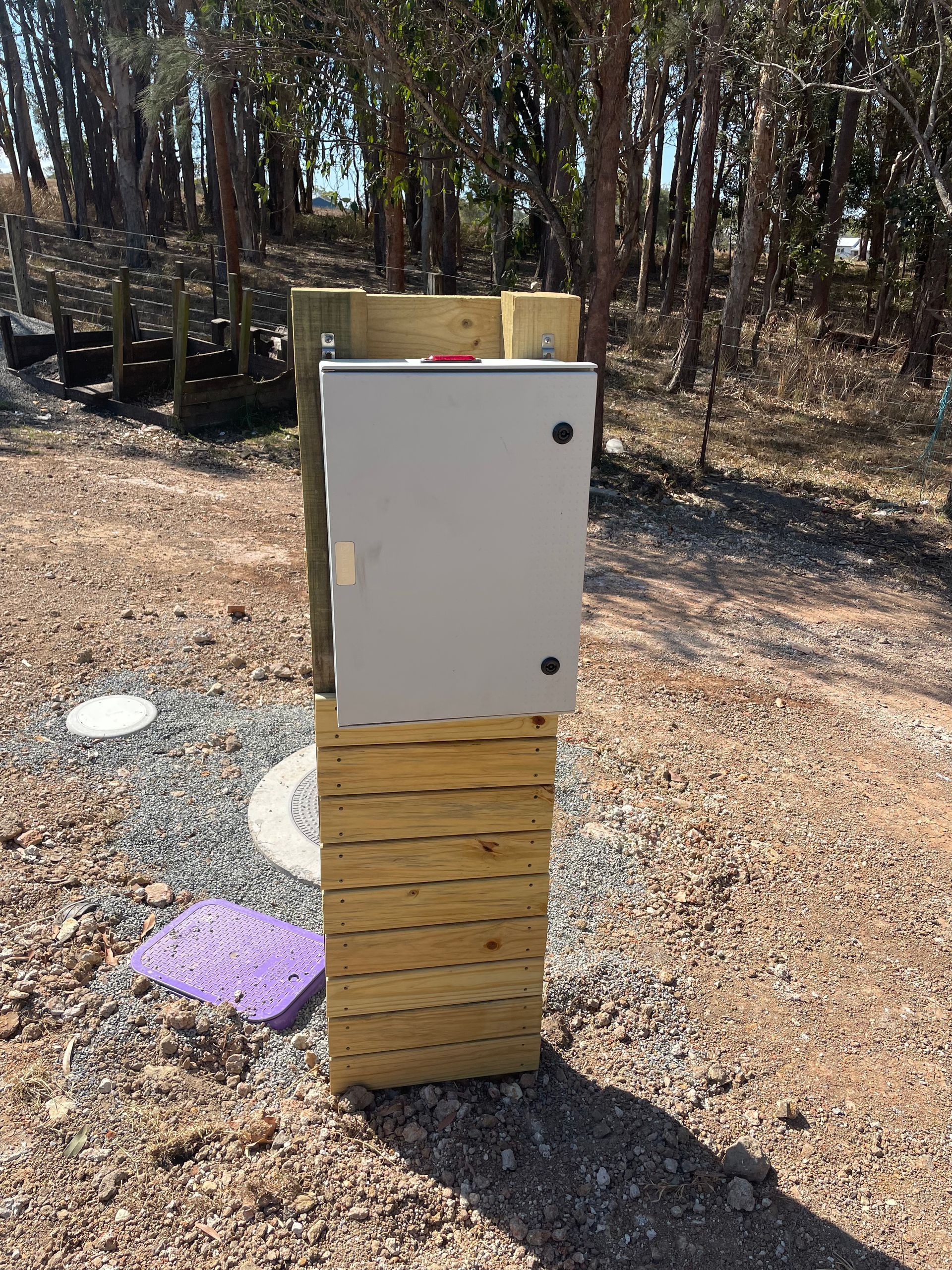 Metal electrical box mounted on a wooden post outdoors, gravel ground, trees in the background— VR Marsden Plumbing in Red Rock, NSW