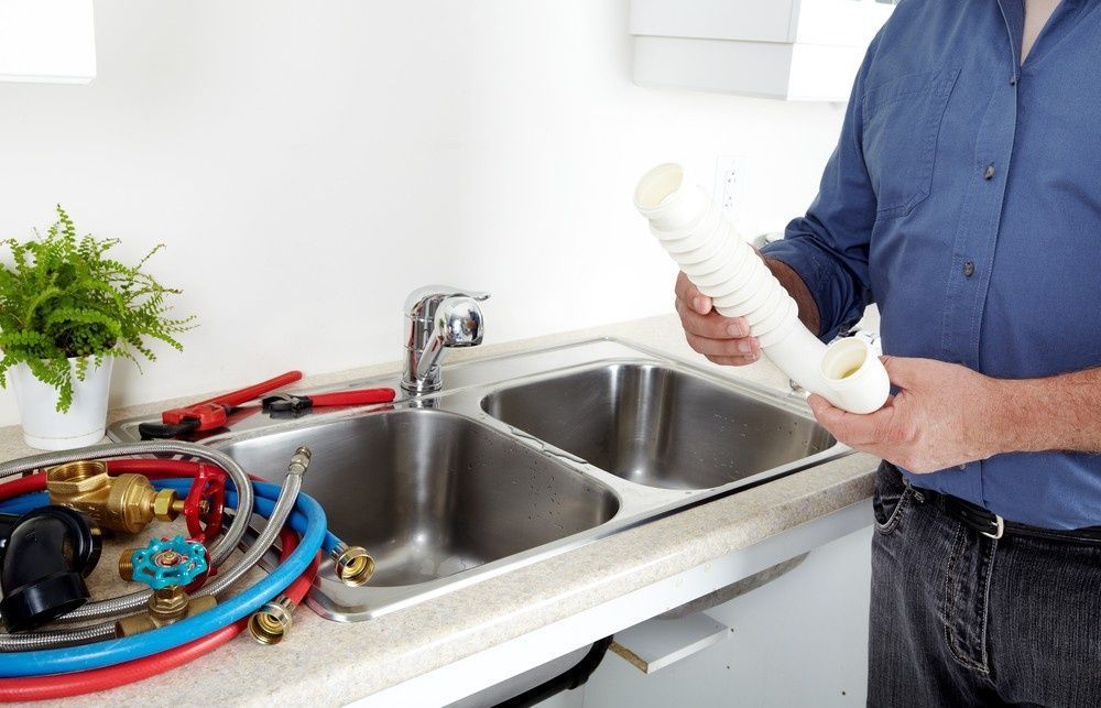 Plumber Near a Kitchen Sink, Holding Pipes — VR Marsden Plumbing in Red Rock, NSW