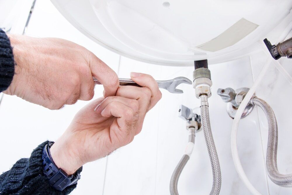Person Using a Wrench to Repair a White Water Heater, in a Bright Setting — VR Marsden Plumbing in Emerald Beach, NSW