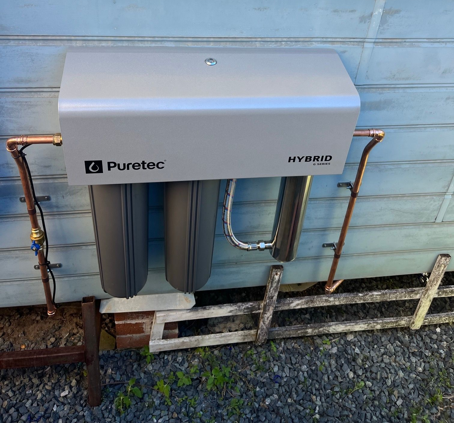 A water filtration system installed on a blue wooden wall with copper pipes— VR Marsden Plumbing in Red Rock, NSW