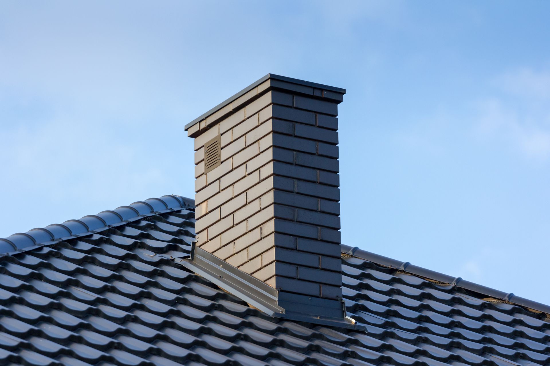 Brick chimney on a gray tiled roof against a blue sky