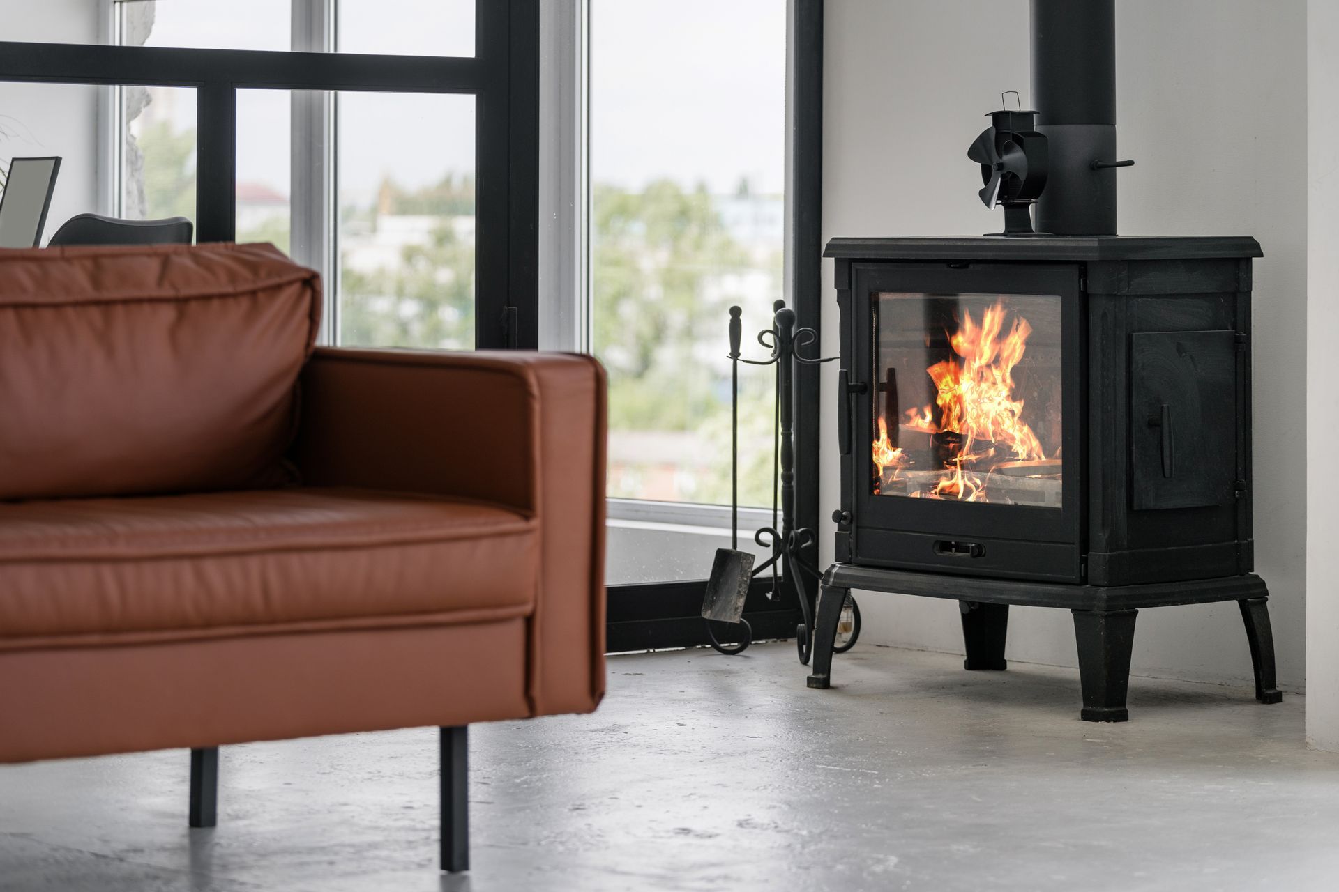 Modern living room with brown sofa and lit black wood stove by large windows