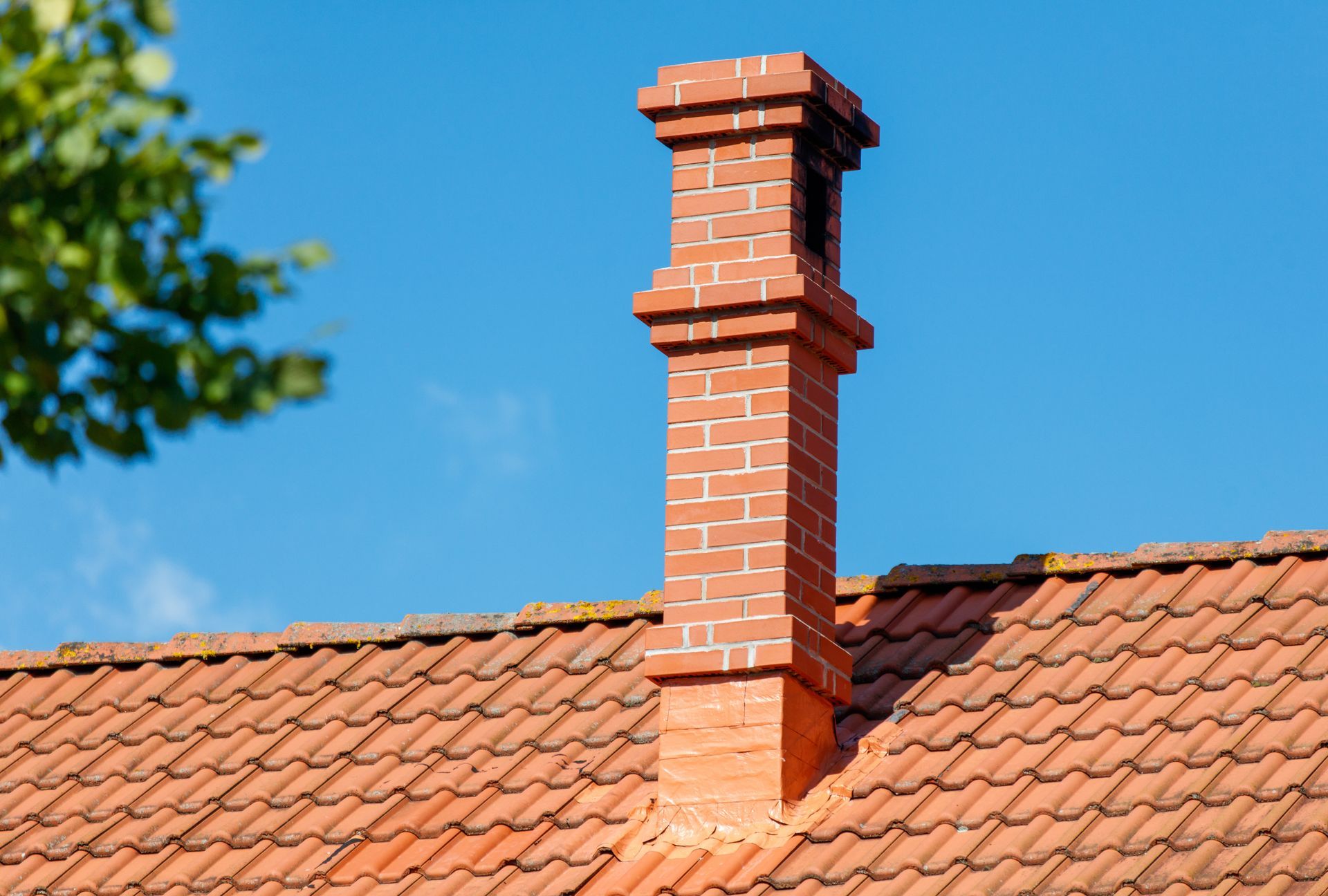 Red brick chimney on a terracotta tiled roof against a blue sky