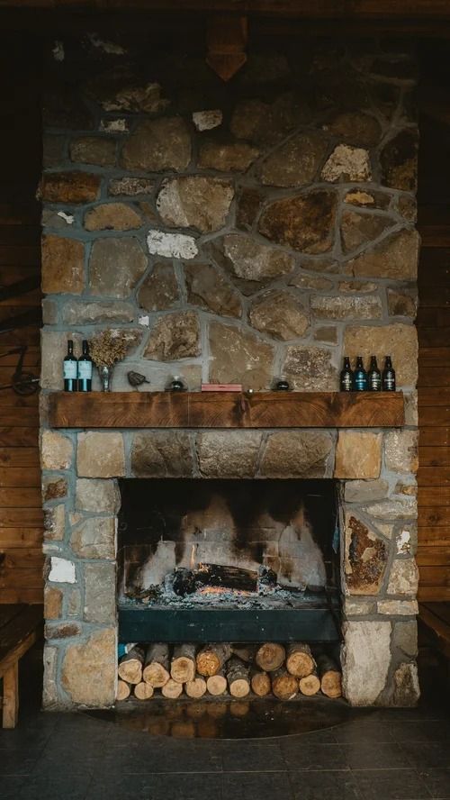Stone fireplace with a wooden mantel, stacked logs, and bottles on either side