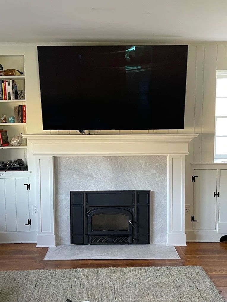 Living room fireplace with wall-mounted TV, white built-in shelves, and hardwood floor