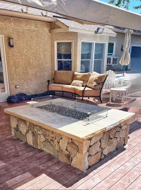 Patio with stone fire pit, sofa, and table beside a stucco house