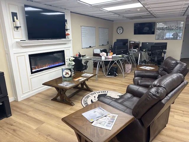 Modern living room with fireplace, TV, leather recliners, coffee tables, and dining area in the background