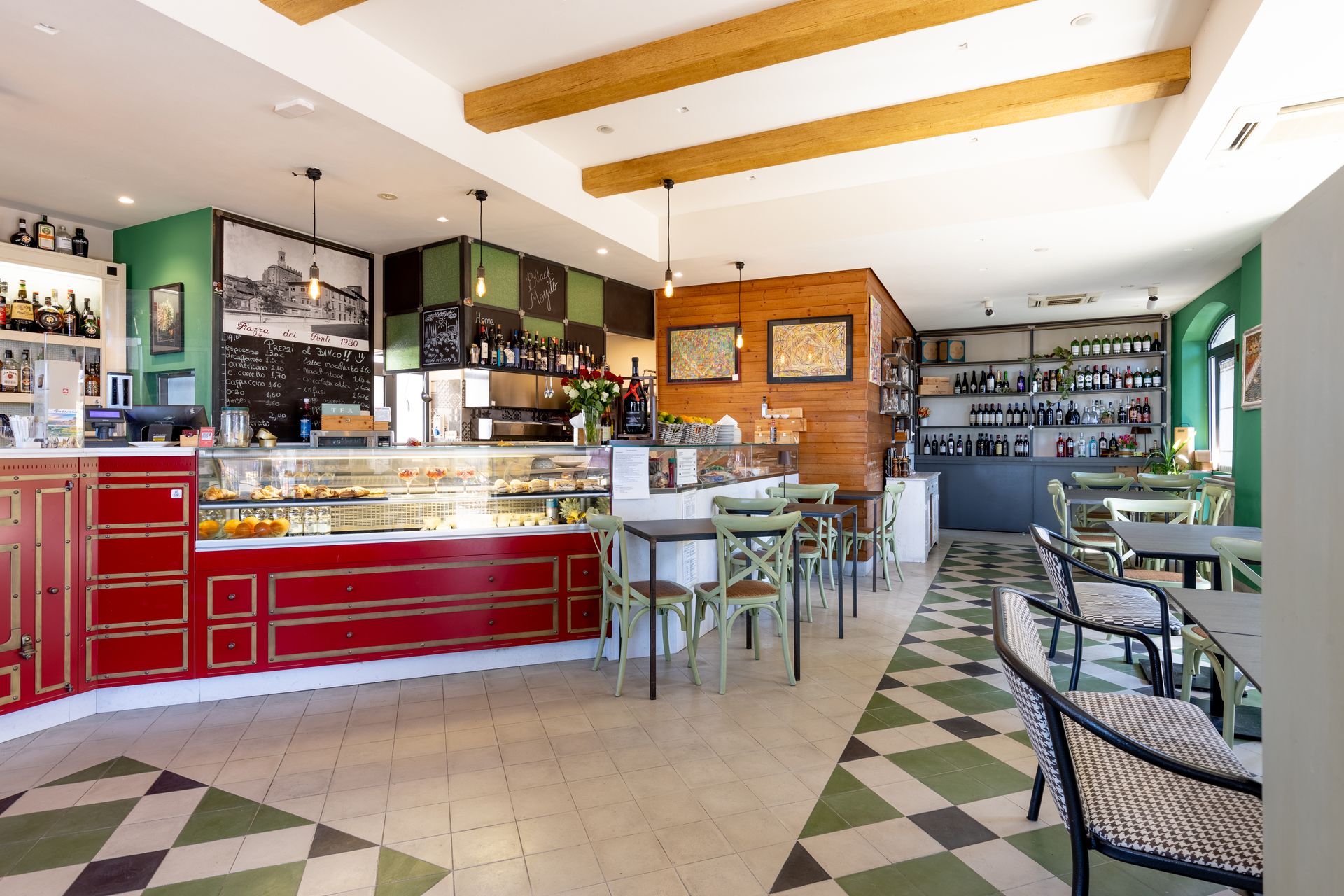 Luminoso interno del caffè con bancone rosso, pareti verdi, tavoli e pavimento piastrellato con motivi decorativi.