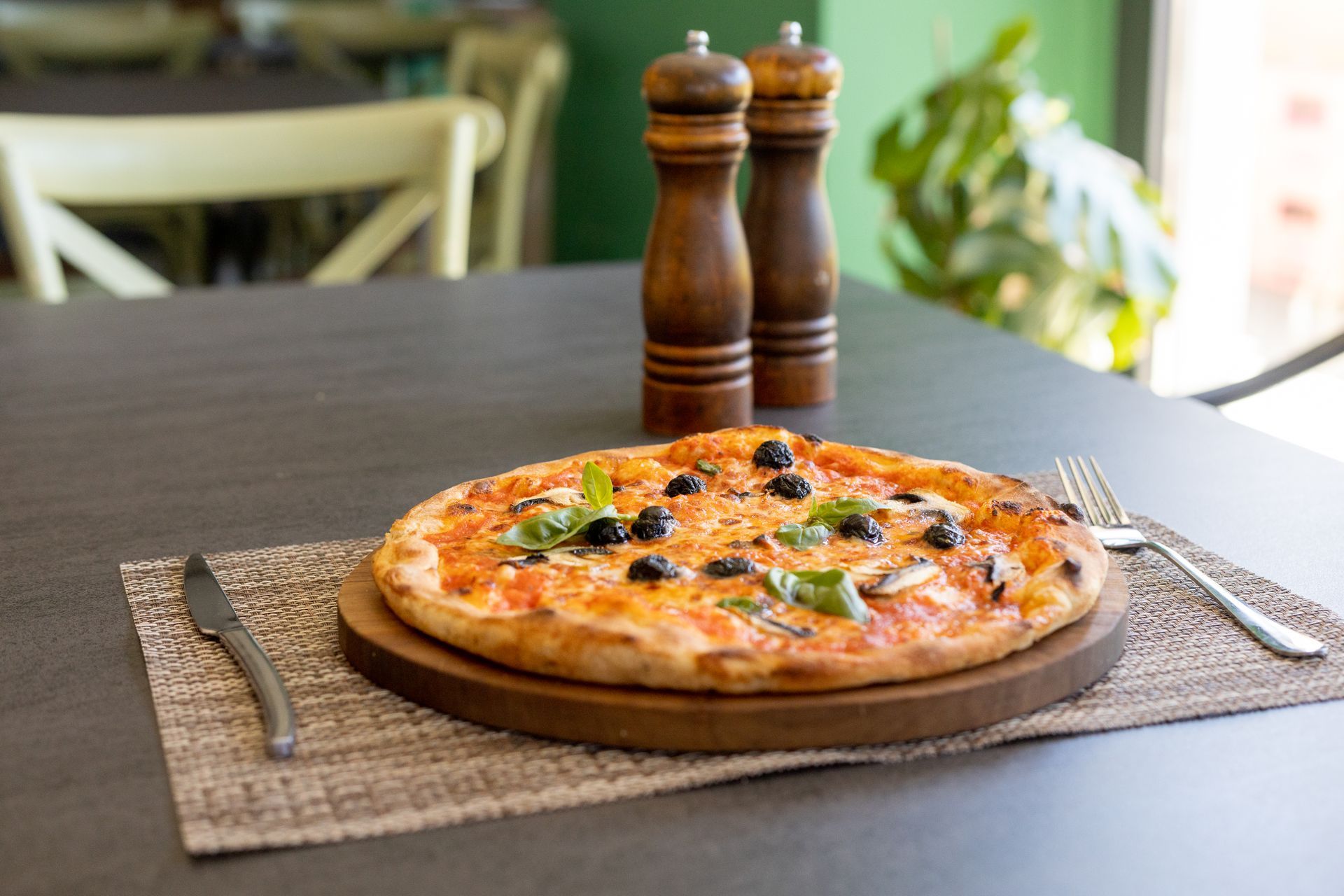 Pizza su un tagliere di legno con macinapepe e coltello su un tavolo da pranzo