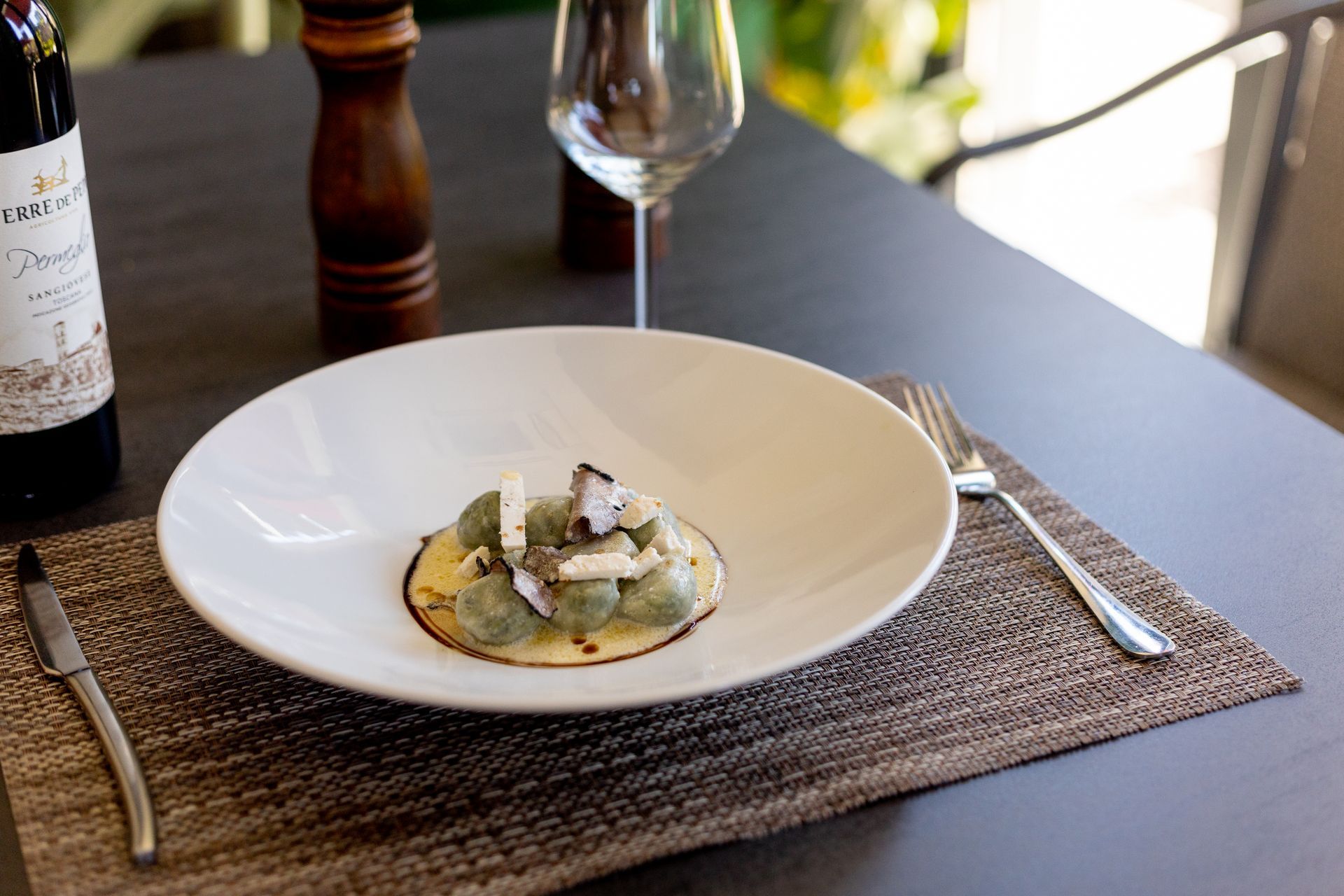 Piatto gourmet impiattato su un tavolo da pranzo con calice da vino, posate e tovaglietta intrecciata.