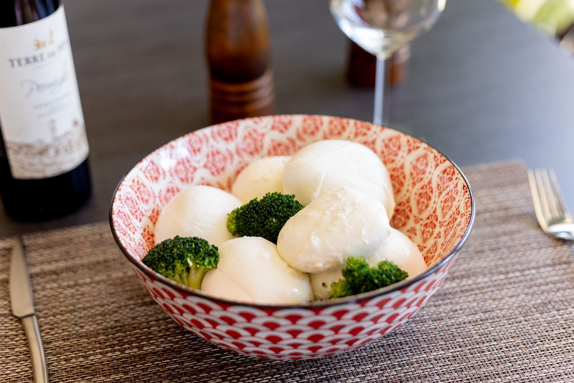 Gnocchi bianchi e broccoli in una ciotola decorata su un tavolo con bottiglie di vino sullo sfondo.