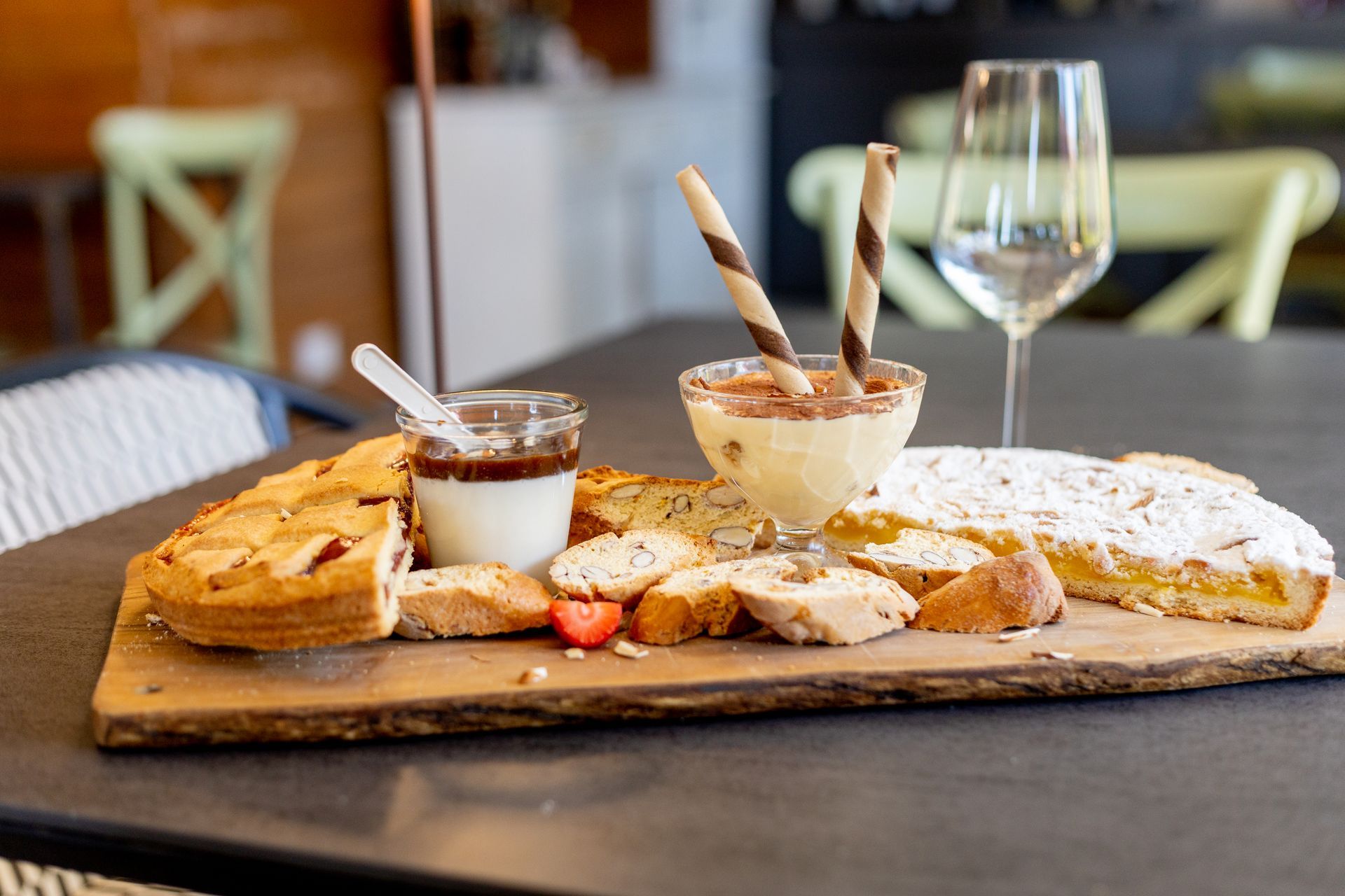 Pane e pasticcini su un tagliere di legno con creme spalmabili, cialde e un bicchiere di vino su un tavolo