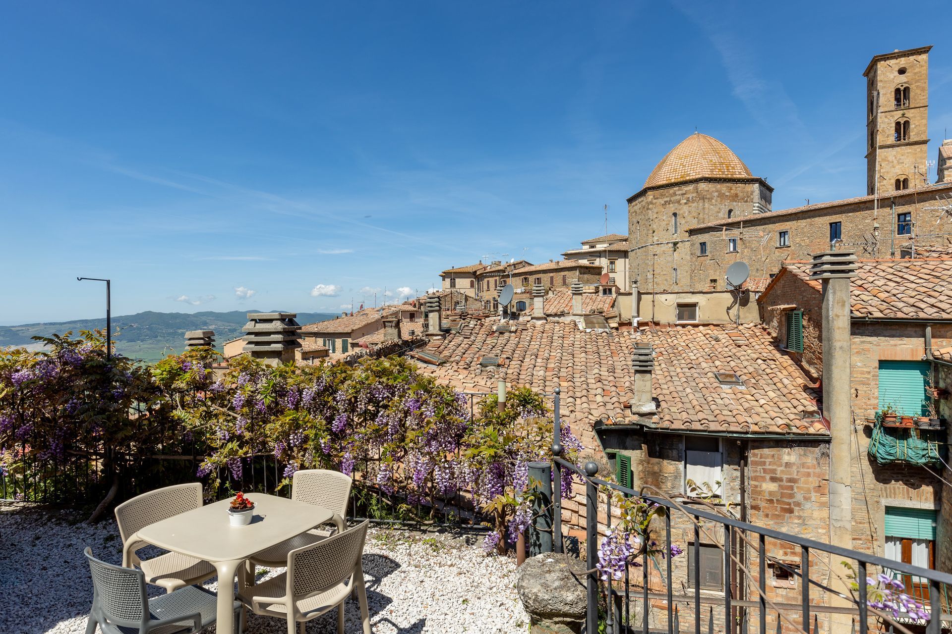Terrazza in pietra affacciata su un borgo storico collinare sotto un cielo azzurro e limpido.