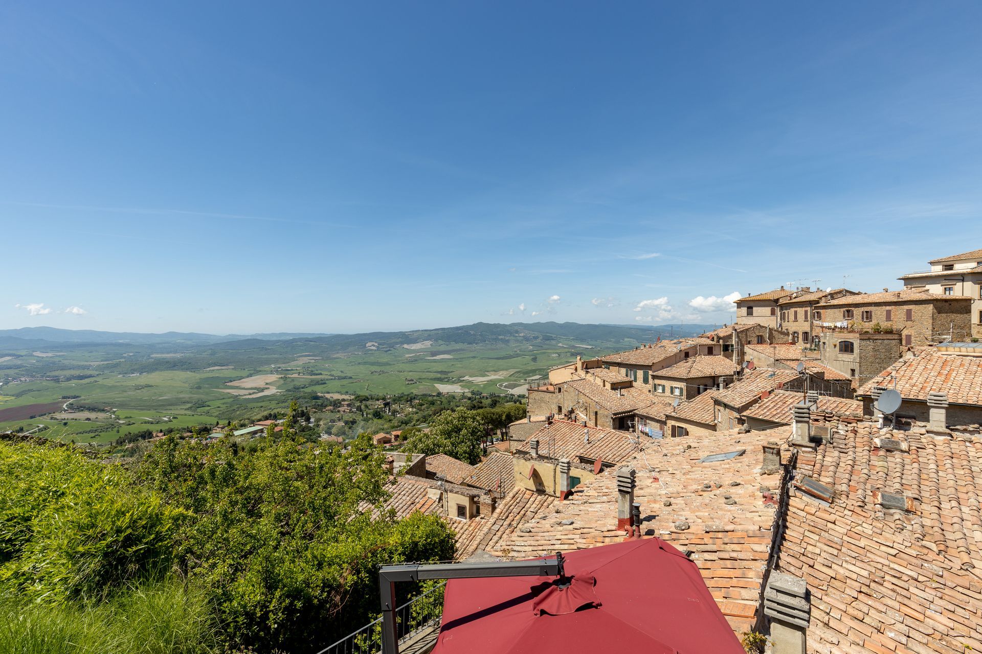 Vista panoramica di un villaggio in cima a una collina con tetti di terracotta che si affaccia su una verde vallata sotto un cielo azzurro.
