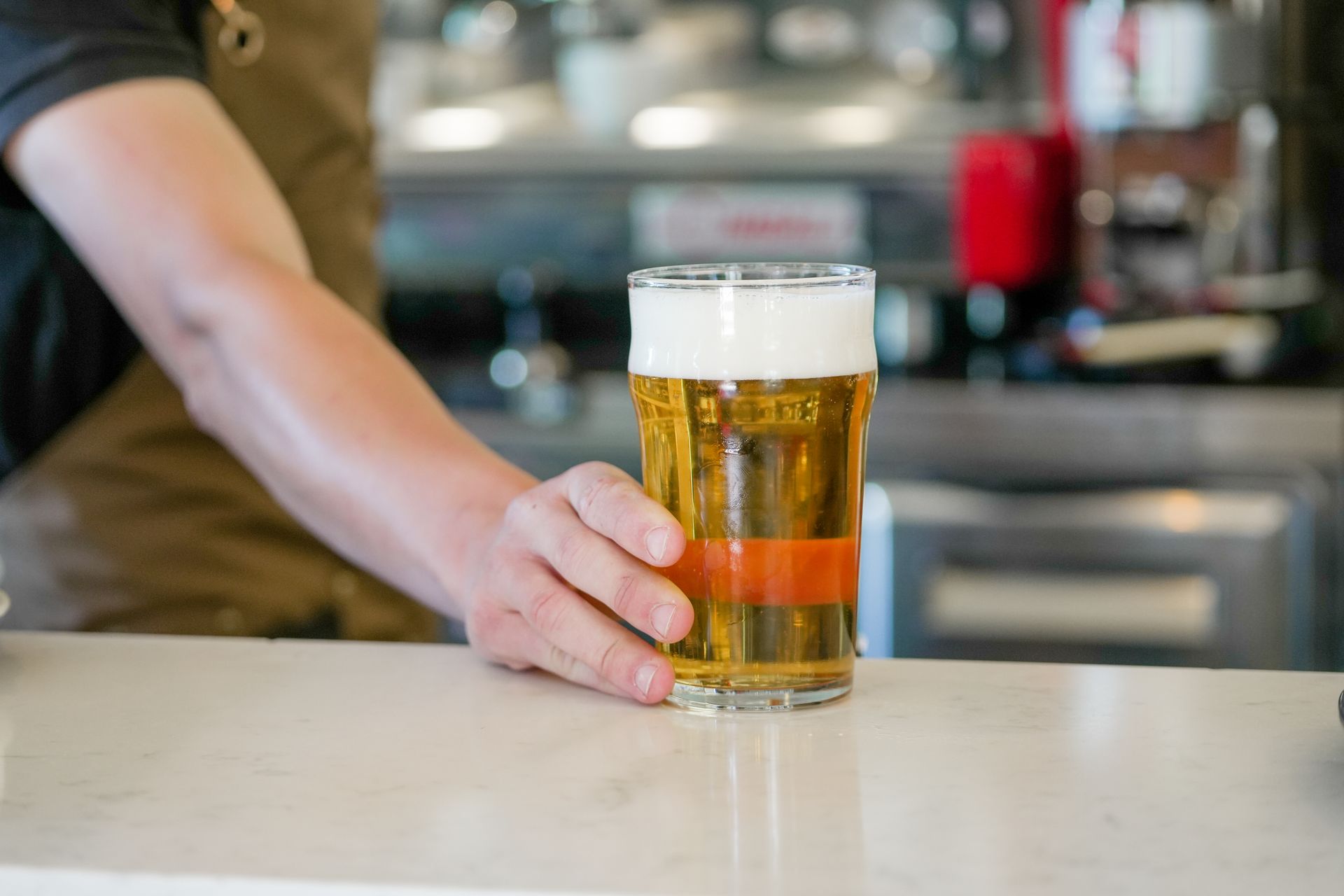 Una mano appoggia una pinta di birra sul bancone di un bar, con uno sfondo sfocato di un pub.