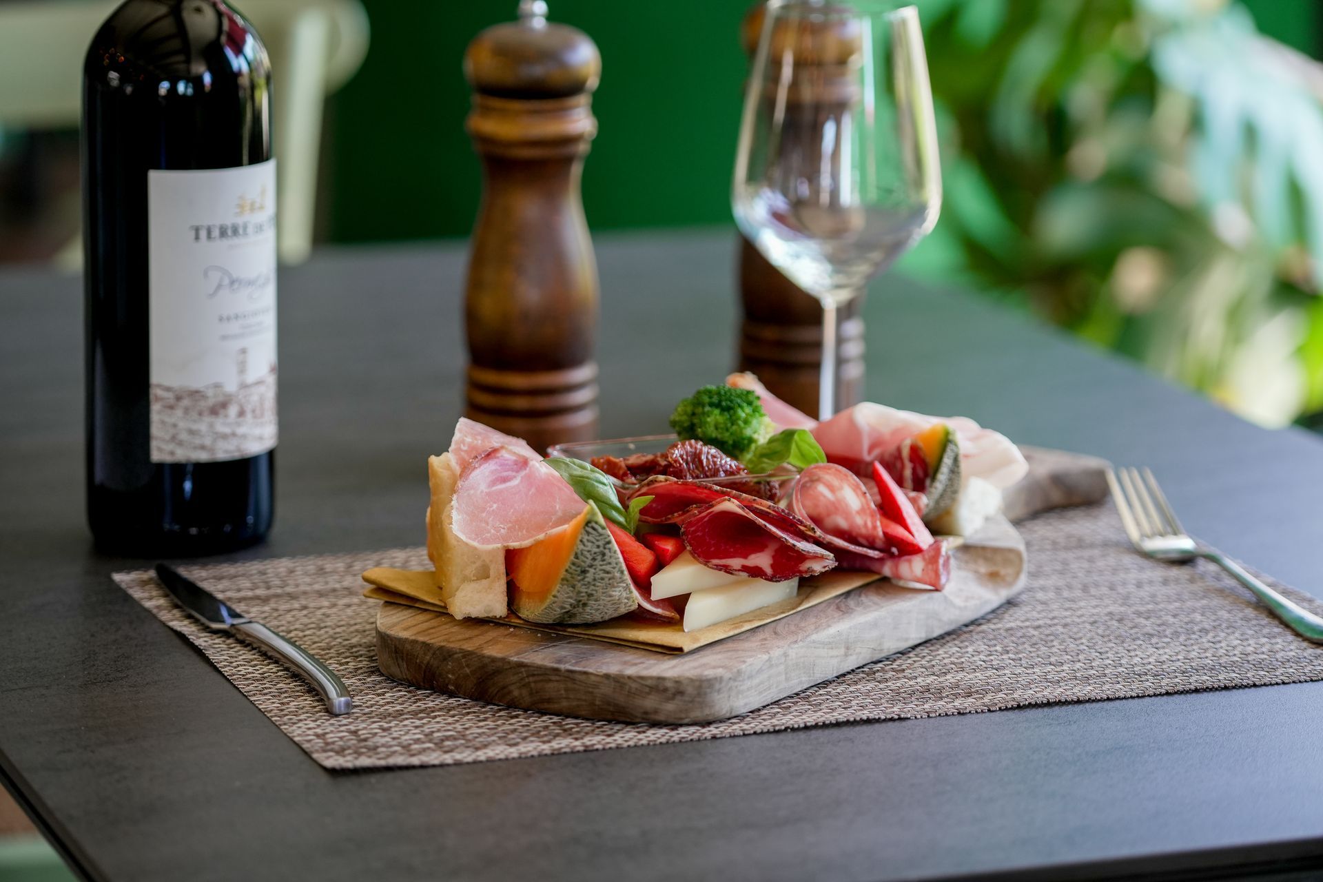 Bottiglia di vino e bicchiere accanto a un piatto di salumi e formaggi su un tavolo da pranzo