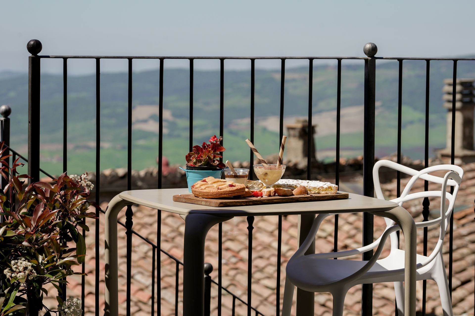 Tavolino da terrazza all'aperto con pasticcini e caffè, affacciato su una pittoresca valle dietro una ringhiera nera.
