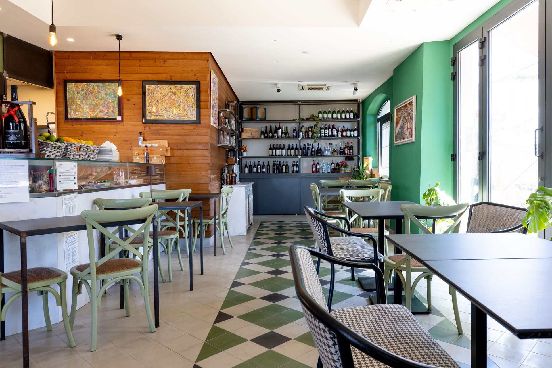 Interno luminoso del caffè con pareti verdi, pavimento piastrellato, tavoli, sedie e un bancone bar sul retro.