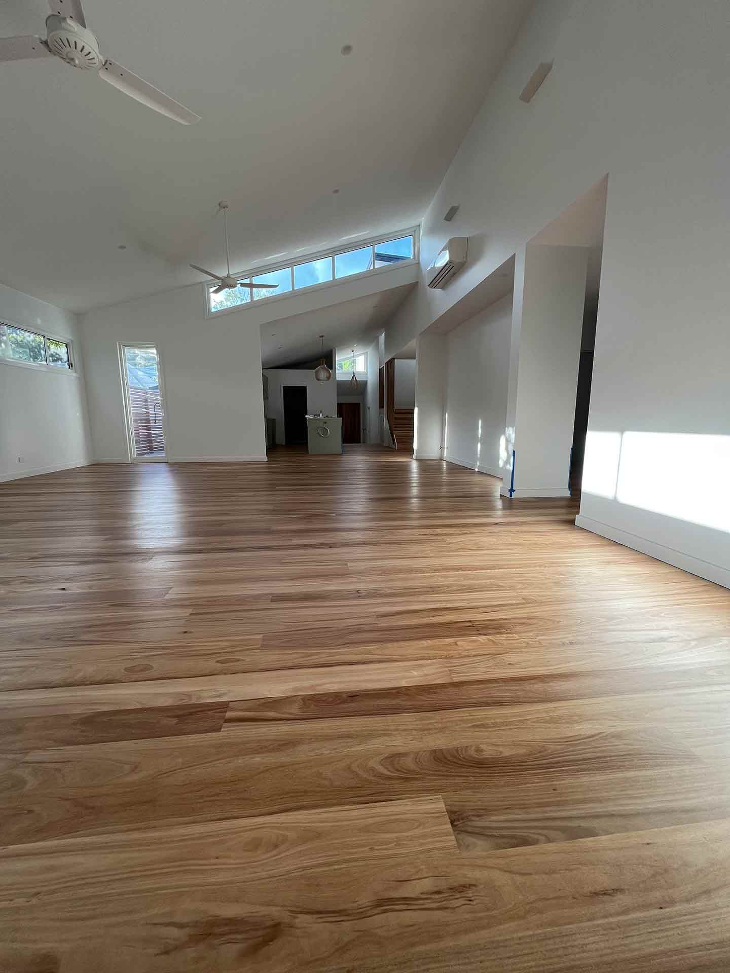 A Large Empty Room With Hardwood Floors and a Ceiling Fan — Hart Projects Wollongong In Dapto, NSW